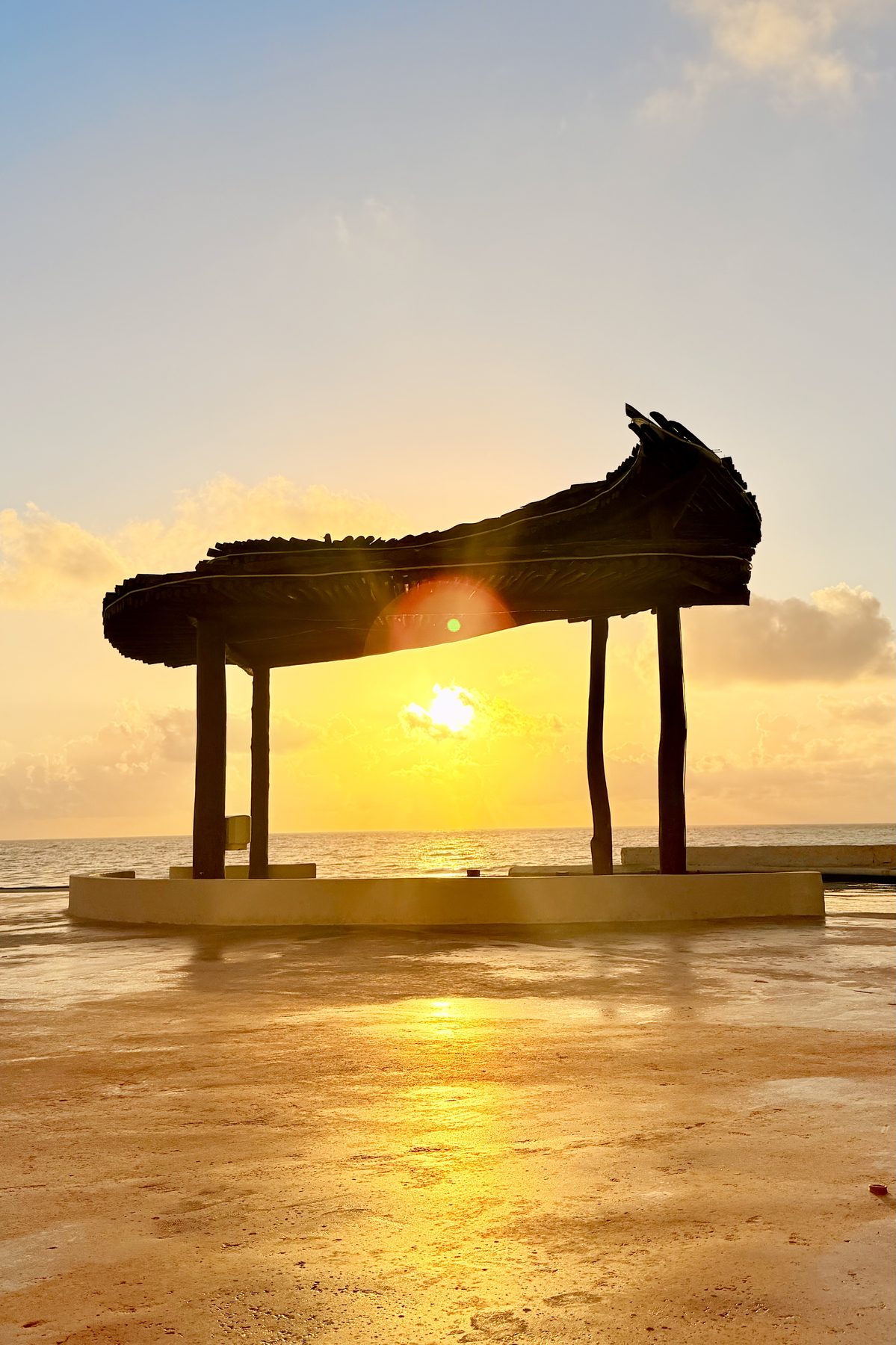 Late afternoon light shifting from cyan toward gold by the water, under a palapa on the shore